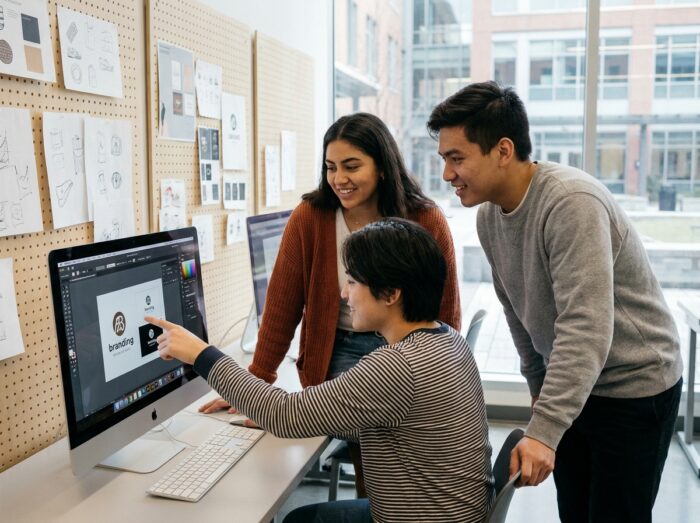 Groupe d'étudiants en école de design graphique collaborant sur un projet de branding sur ordinateur dans une salle de cours moderne